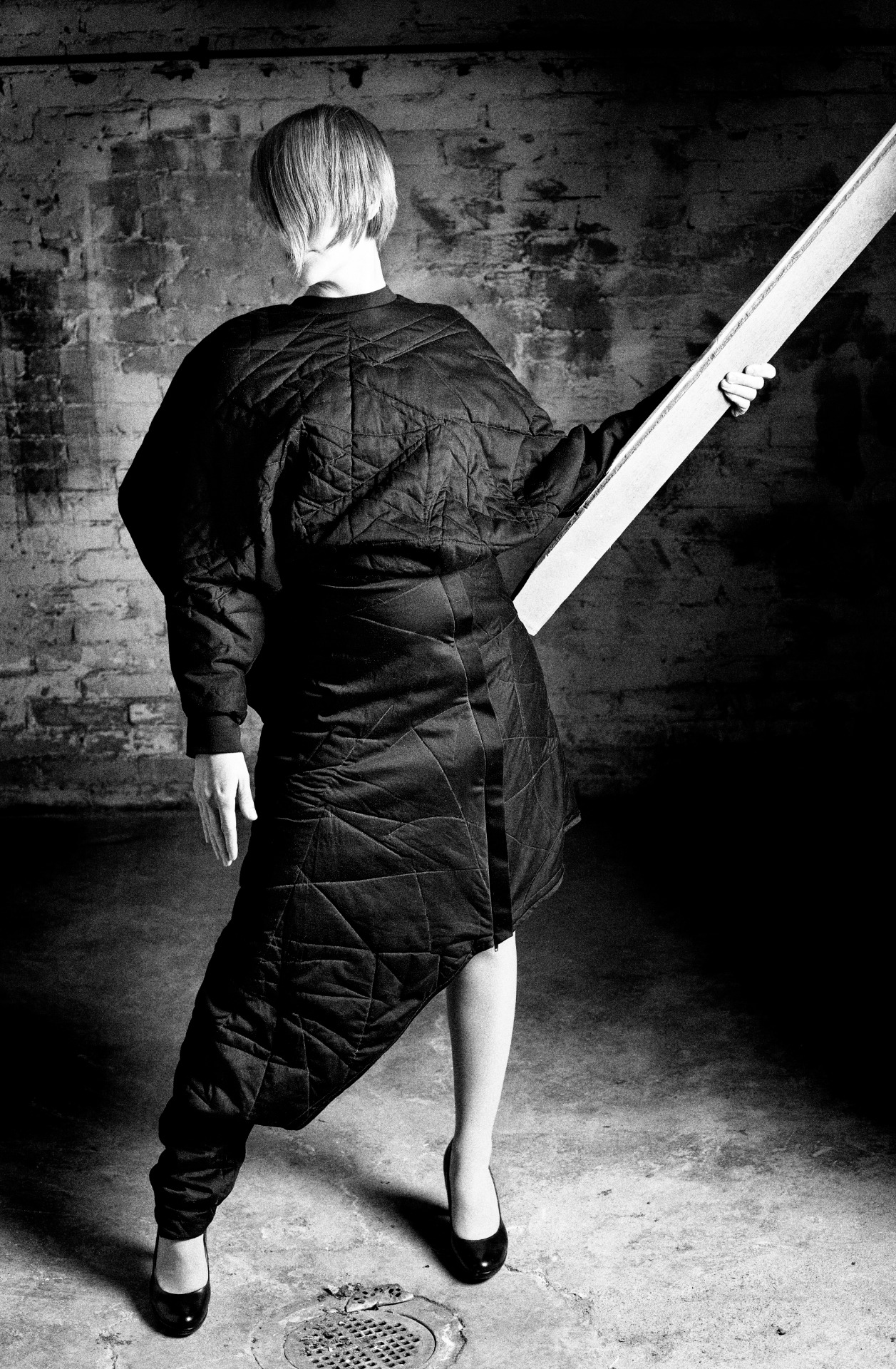 Henkilö seisoo kameran suuntaan ja hiukset kasvojen edessä yllään kahdesta yhdestä kappaleesta rakennetusta vaatteesta koostuva asu: tilava paita ja epäsymmetrinen yhden lahkeen housuhame.