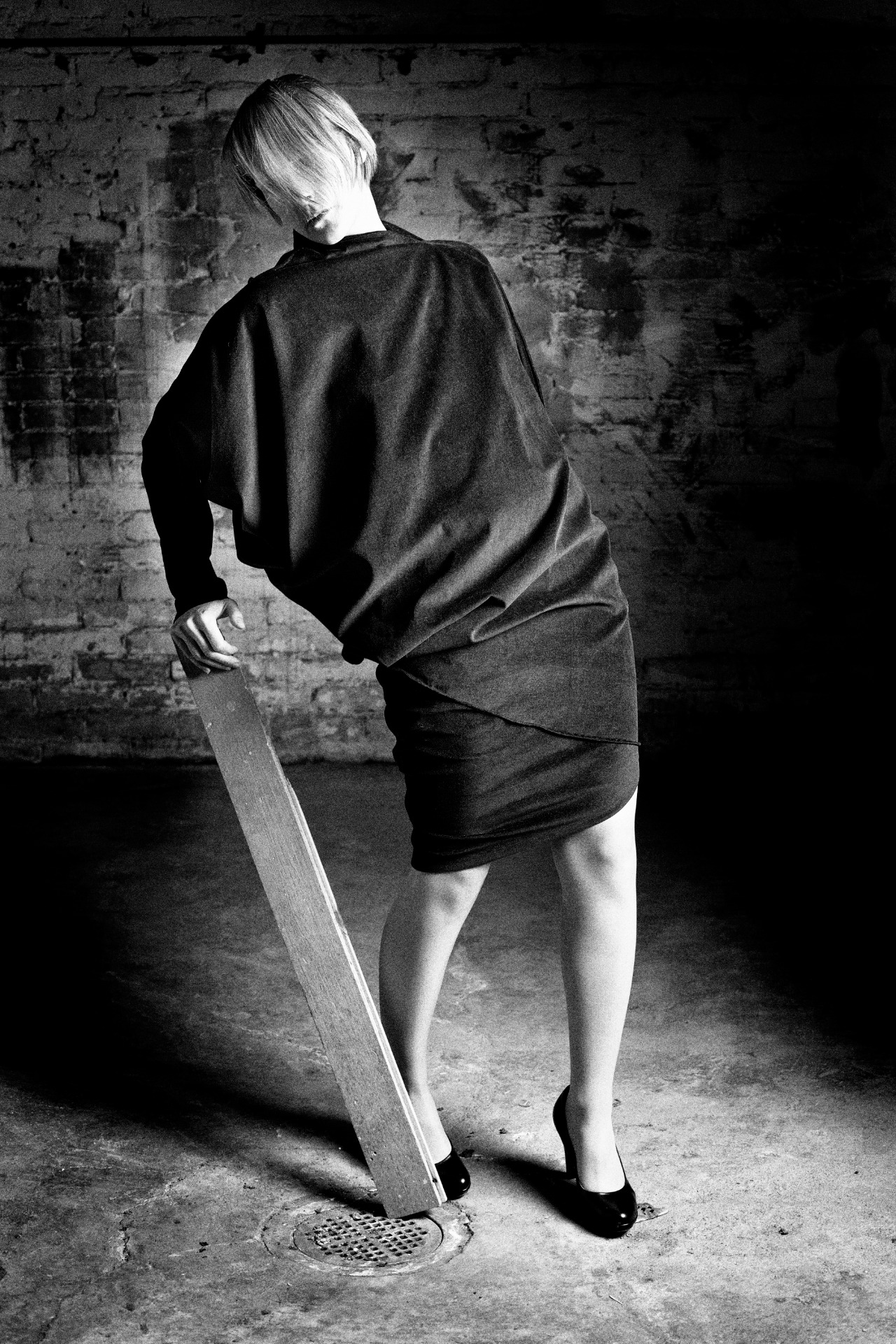 Henkilö seisoo hieman kääntyneenä, yllään yhdestä kappaleesta valmistettu samettinen vaate, joka muodostaa yläosan ja kietoutuvan hameen.