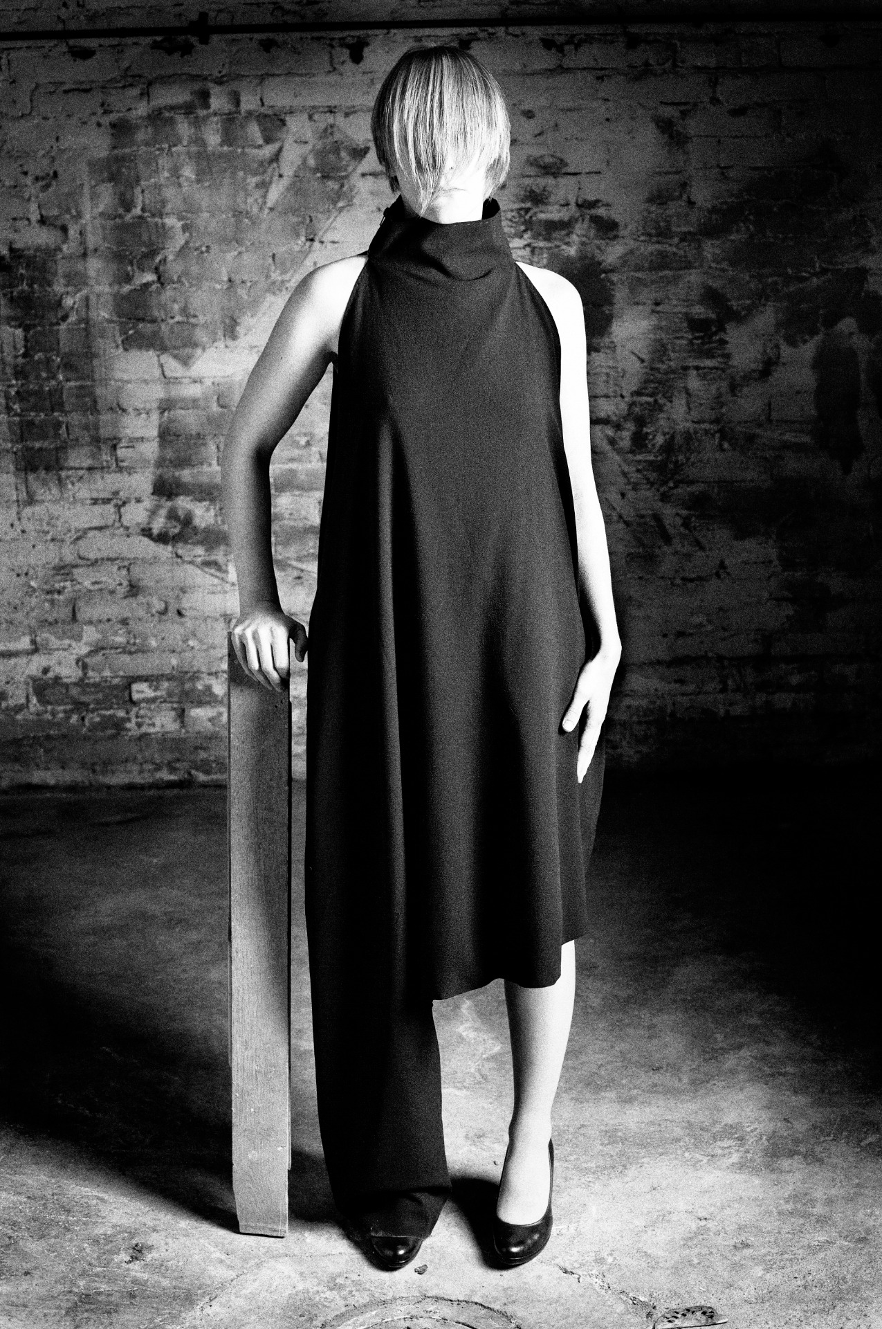 Henkilö seisoo suorassa villakrepistä valmistetussa mekossa, joka on toteutettu kahdesta kappaleesta ja laskeutuu epäsymmetrisesti.